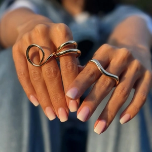 Close-up of golden irregular spiral and wave rings worn on fingers in warm sunlight