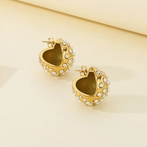 Close-up of golden heart earrings with white faux pearl embellishments and metal texture