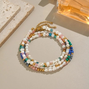 Detail of layered bracelet set with irregular pearls and colorful beads on beige surface