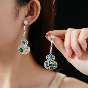 Detail of silver drop earrings with green gemstones and sparkling hollow gourd design