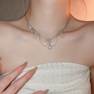 Détail d'un collier à franges argentées avec perle blanche centrale sur col en dentelle
