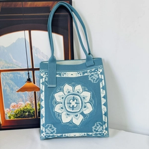 Detail of blue knit tote bag with lotus pattern resting against a wall art backdrop