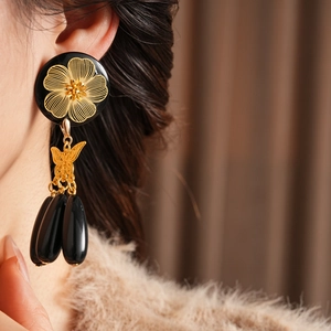 Detail of vintage gold flower butterfly earrings with black teardrop beads on a model
