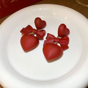 Detail of red matte earrings with bow and heart shapes on a ceramic plate