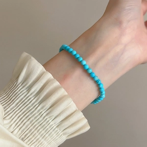 Close-up of a minimalist turquoise beaded elastic bracelet worn on a female wrist