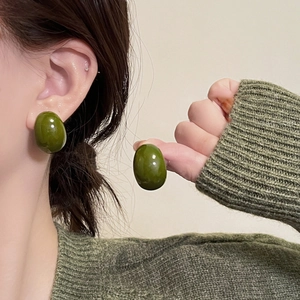 Detailed close-up of dark green olive-shaped resin stud earrings on model in green knitwear