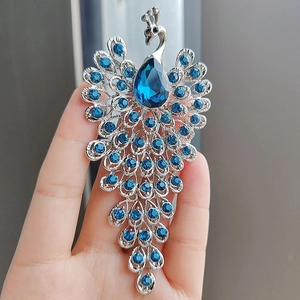 Elegant peacock brooch pin with blue crystal water drop and rhinestones held in hand