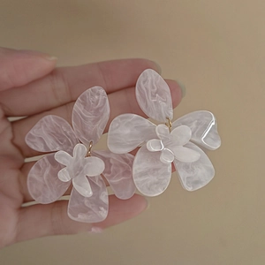 Detail view of white resin flower earring with marble texture held by hand