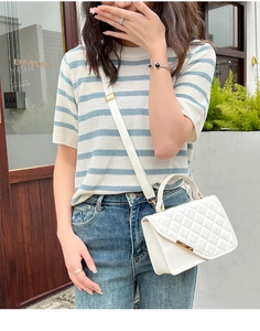 Detail of white quilted crossbody bag with gold metal trim and chain shoulder strap
