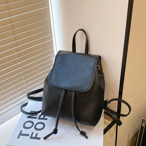 Minimalist black faux leather backpack with drawstring closure and flap on book prop