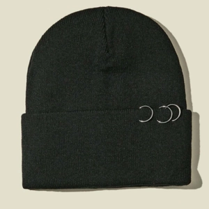 Détail du bonnet en maille noire avec trois anneaux métalliques argentés sur le bord
