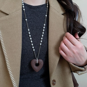 Detail of a large textured brown heart pendant with a pearl bead necklace on a sweater