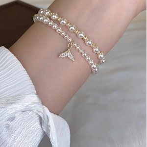 Close-up of double-layer pearl bracelet with a gold-plated zircon fishtail pendant