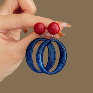 Detail shot of a red bead and blue resin hoop earring held in hand for scale