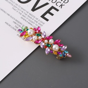 Detail of gold metal hair clip with colorful rhinestones and faux pearls on white paper