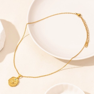 Golden stainless steel necklace with engraved baby footprint pendant on a white plate