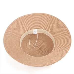 Detail view of straw sun hat interior showing adjustable strap and 100% paper material label