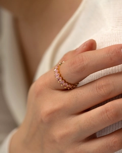 Close-up of elegant gold eternity ring featuring oval-cut pink gemstones on model's finger