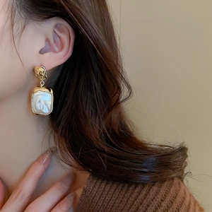 Vintage gold metal earrings with rectangular faux pearl pendants on a model