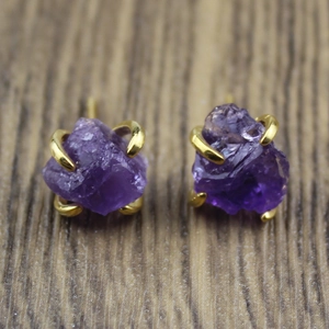 Macro shot of natural purple amethyst raw stone stud earrings with gold-tone claw settings