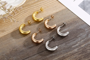 Detailed view of C-shaped hoop earrings in gold, rose gold and silver on a textured surface