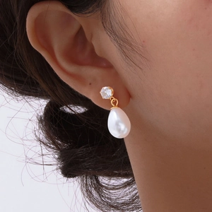 Close-up of golden teardrop pearl earrings with clear zircon stones on a model