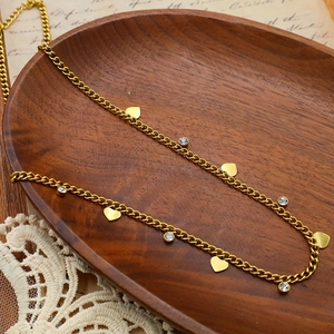 Elegant gold titanium necklace with heart charms and zircon insets on wooden tray