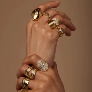 Golden titanium steel ring set with zircon inlay on model hand over warm brown background