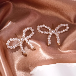 Close-up of bow-shaped pearl earrings on a luxurious rose gold silk fabric background