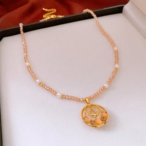Détail du collier de perles champagne et pendentif double anneau doré orné de zircons