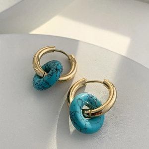 Detailed view of 18K gold earrings with round turquoise stone pendants on grey background