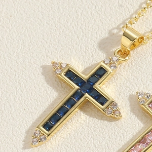 Macro shot of gold cross pendant featuring blue square zircons and white round crystals