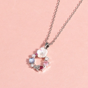 Détail du collier argenté avec pendentif couronne florale, perles et petit papillon