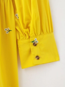 Close-up detail of white floral embroidery and resin buttons on yellow shirt cuff