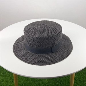 Detailed texture of dark grey woven straw boater hat with black ribbon on a white table