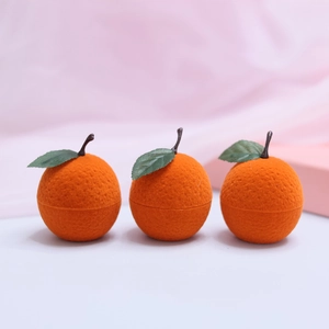 Three cute orange-shaped velvet jewelry boxes with green leaves on a soft pink background