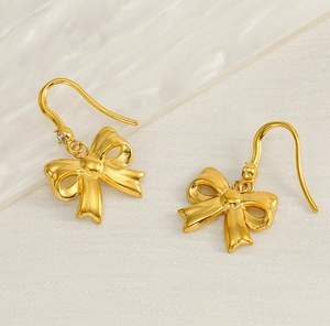 Detailed close-up of gold bow earrings in matte finish on soft cream textured background