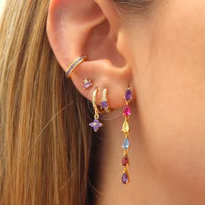 Detail of model wearing gold hoop earrings set with colorful zircon and purple crystal