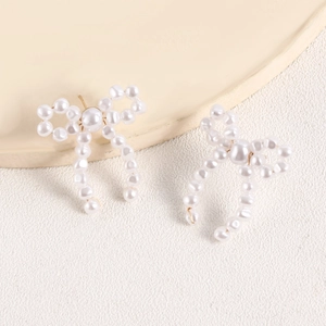 Detail of handmade bow-shaped pearl earrings with cream finish and vintage gold posts