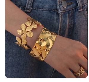 Detailed view of gold textured cuff bracelet and floral jewelry on denim background