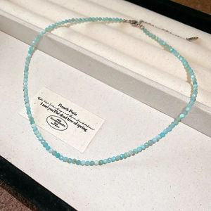 Macro detail of faceted light blue bead necklace with adjustable silver clasp and logo tag