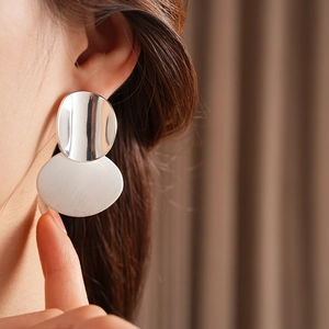 Close-up of minimalist silver oval brushed metal earrings worn by a model