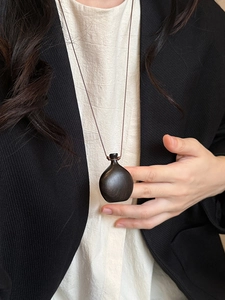 Detail view of the brown wood bottle pendant on a minimalist long sweater necklace