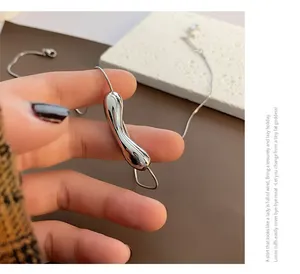 Macro detail of silver irregular curved drop pendant on a thin snake chain necklace