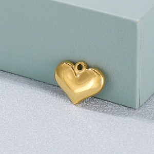 Close-up of a polished gold 3D heart pendant on a textured surface