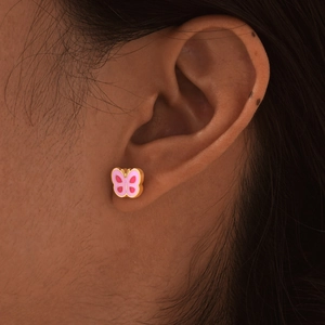 Detail of a pink butterfly stud earring worn on earlobe with gold metal plating