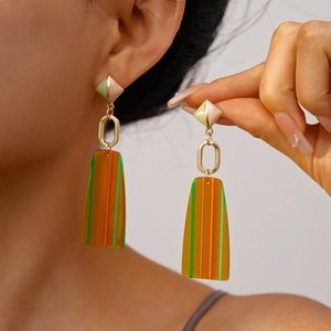 Detail of model wearing geometric resin drop earrings with color-block rhombus and stripes