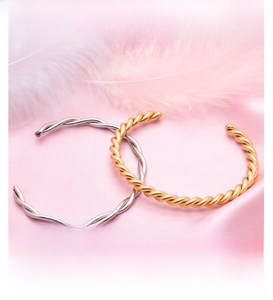 Detailed view of twisted wave bangles in gold and silver finish on pink satin