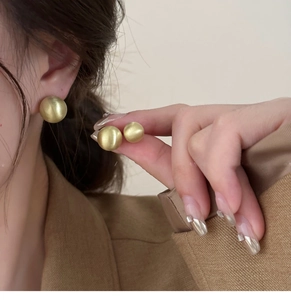 Close-up of matte gold round ball stud earrings showing brushed metal texture and size scale