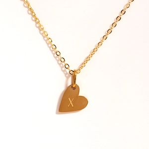 Détail du collier pendentif coeur doré avec une lettre X gravée sur du métal poli
